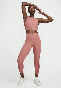 Svetloružový športový podprsenka a zodpovedajúce legíny. Tkanina je hladká s jemným leskom, so subtílnym brandingom na páse.