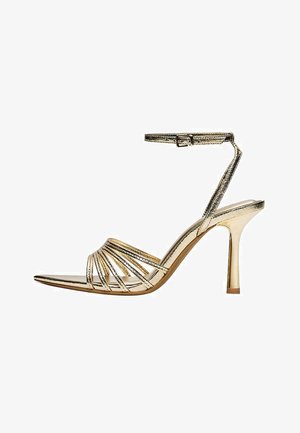 Sandale aurii cu barete, toc înalt cu baretă la gleznă, vârf decupat și toc subțire stiletto pe fundal alb.