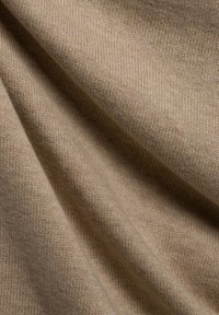Beiger Strickstoff mit feiner Textur, der eine weiche, glatte Oberfläche und sichtbare, subtile ineinandergreifende Stiche aufweist.