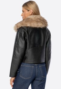 Giacca di pelle nera con colletto in pelliccia sintetica, design corto, texture liscia e cuciture strutturate, abbinata a jeans in denim scuri.