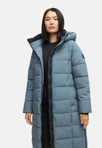 Duga plava puffer jakna s kapuljačom, s kvadratnim uzorkom, dva bočna džepa i crni detalj munje sprijeda.