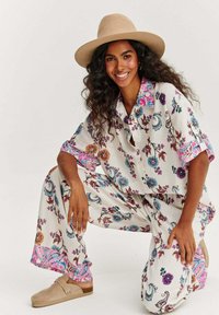 Oblečení z lehké látky s květinovým vzorem, zahrnující košilový top s límečkem a volné kalhoty. Doplněné růžovými a modrými detaily. Béžové slip-on boty.