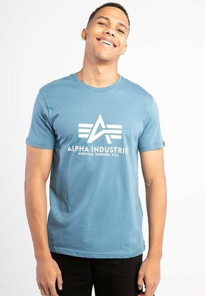 Light blue cotton T-shirt with short sleeves, featuring a white logo and text "ALPHA INDUSTRIE" centered on the front.