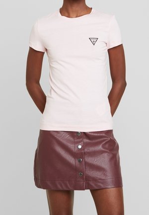 T-shirt en coton rose avec un logo triangulaire noir sur le côté gauche de la poitrine, associée à une mini-jupe en cuir bordeaux avec des boutons en métal.
