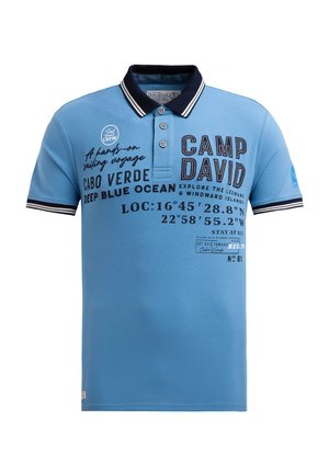 Hellblaues Poloshirt aus Baumwollstoff mit einem dunkelblauen Kragen. Mit aufgedrucktem Text und Grafiken, darunter Koordinaten und Markenname.