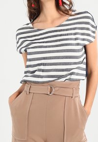Camiseta de rayas en gris y blanco, con escote redondo y mangas cortas. Combinada con pantalones de tiro alto en beige que cuentan con un cinturón con hebilla redonda.
