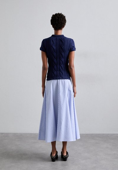 Marineblaues Strickoberteil mit Kabelmuster, kombiniert mit einem hellblau gestreiften Midi-Rock. Schwarze High Heels runden das Outfit ab.