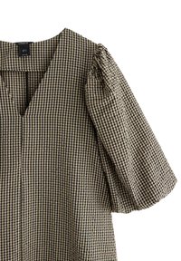 Mönstrad blus med V-ringning och puffärmar, tillverkad av textil med en svart och beige ginghamrutig design.