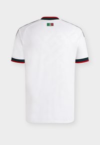 Λευκό πουκάμισο με κοντά μανίκια και μαύρο και κόκκινο περίγραμμα στα μανίκια και το γιακά, μικρό πράσινο και κόκκινο λογότυπο με μοτίβο στο κέντρο κάτω από τον γιακά στην πλάτη.