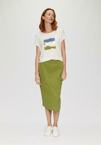 T-shirt blanc avec des motifs abstraits bleu, argent et vert, associé à une jupe cargo olive à mi-cuisse et des baskets blanches.