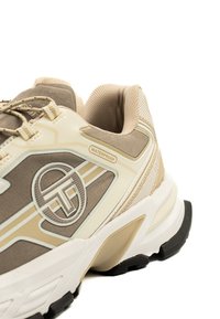 Vattentät sportskor i beige och kräm, med överdel i mesh och textil, dämpad sula och distinkt logotyp på sidan.