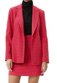 Różowa marynarka w wzór houndstooth w komplecie ze spódnicą, z klapami i kontrastowym czarnym golfem pod spodem.