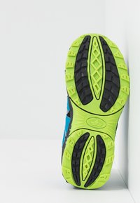 Zapatilla de running con una suela negra texturizada, acentos verde brillante y un upper azul con superposiciones en negro y gris.
