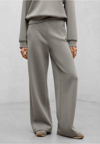 Pantaloni a gamba larga e vita alta in tessuto grigio chiaro. Presentano una texture liscia con cuciture laterali, un design semplice e una vestibilità comoda.