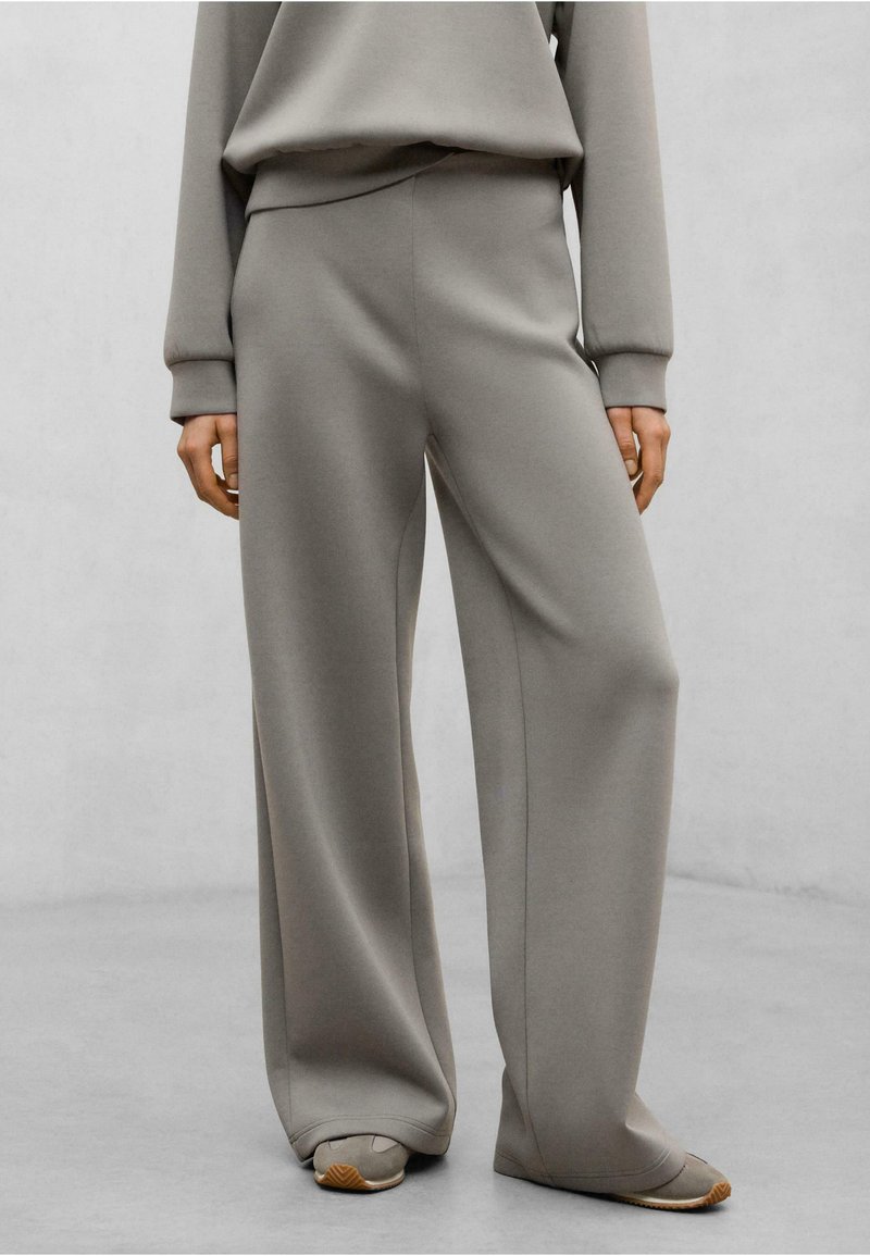 Pantaloni a gamba larga e vita alta in tessuto grigio chiaro. Presentano una texture liscia con cuciture laterali, un design semplice e una vestibilità comoda.