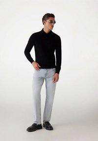 Polo noir à manches longues associé à un jean bleu clair et des chaussures noires épaisses. Le modèle porte également des lunettes de soleil grises.