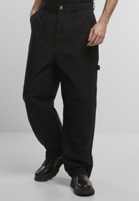 Fekete pamut cargo nadrág, laza szabással, elülső zsebekkel és texturált felülettel. Fekete bőr csizmával párosítva.