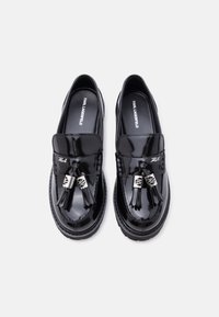 Ζευγάρι γυαλιστερών μαύρων μοκασίνων Karl Lagerfeld με φούντες και ασημένιες λεπτομέρειες σε απλό λευκό φόντο.