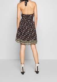 Czarna sukienka z dekoltem halter, wzorzysta na czerwono i biało, z dekoracyjną złotą lamówką na dole. Połączona ze srebrnymi botkami za kostkę.