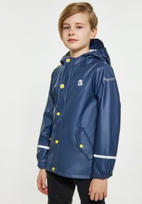 Ūdensizturīgs tumši zils lietus mētelis ar priekšējo rāvējslēdzēju, dzeltenām pogām, baltām akcentiem un kapuci. Iekļauj sānu kabatas un logotipu uz piedurknes.