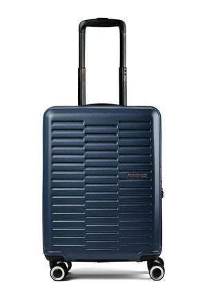 Maleta rígida azul marino con relieves horizontales, asa negra retráctil, cuatro ruedas giratorias y logo de American Tourister en el frontal.