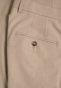 Beige trousers featuring a rear pocket with a button closure. Material has a smooth texture with a subtle, woven design.