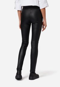 Zwarte nepleer legging met een aansluitend ontwerp en hoge taille. Glad textuur, enkellang, gecombineerd met zwarte schoenen.