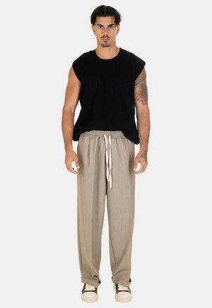 Top smanicato nero a coste e pantaloni beige con coulisse. Modello che indossa sneaker bianche con accenti neri. Sfondo semplice.