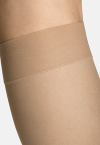 Beige Oberschenkelstrümpfe mit glatter, matter Textur und einem breiten, elastischen Bündchen oben für einen sicheren Sitz. Nahtloses Design.