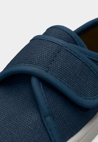 Gros plan d'une chaussure en tissu bleu marine avec une large bride réglable en Velcro et un détail de couture texturée.