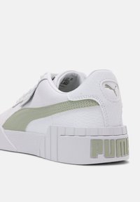Bílé kožené tenisky se světle zelenými akcenty, silnou podrážkou, strukturovaným povrchem a výrazně zobrazeným logem "PUMA" na patě.