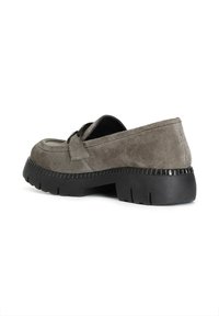 Mocasines de ante gris con una suela de goma negra baja y gruesa. Presenta una correa decorativa en la parte delantera y un acabado texturizado a lo largo de la suela.