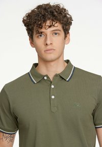 Grøn polo t-shirt med tekstureret stof, der har en to-knap lukning, kontraststribede krave og ærmer samt et broderet logo.