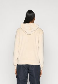 Beżowa bluza z kapturem o luźnym kroju, z kangurkową kieszenią i ściągaczami przy mankietach. Gładka faktura i prosty design.
