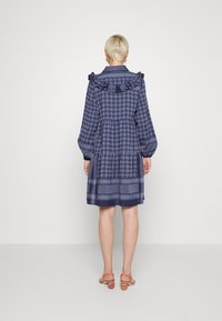 Granatowa sukienka w wzór w houndstooth, z falbanistym kołnierzykiem i długimi, bufiastymi rękawami, z warstwowanymi sekcjami i dekoracyjnym wykończeniem.