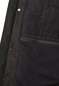 Schwarzer, gesteppten Stoff mit glatter Textur, ausgestattet mit einer Reißverschluss-Netztasche und Druckknopfverschlüssen. Das Design hat eine vertikale Ausrichtung und dezente Akzente.