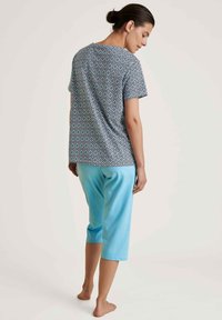 Patroon katoenen t-shirt met korte mouwen, gecombineerd met lichtblauwe, knielange broeken, weergegeven vanaf de achterkant. Zachte textuur, casual pasvorm.