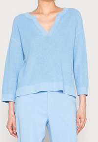 Maglione a coste di colore azzurro chiaro, con scollo a V e maniche a tre quarti. Presenta un design rilassato e ampio, con un orlo leggermente più lungo sul retro.