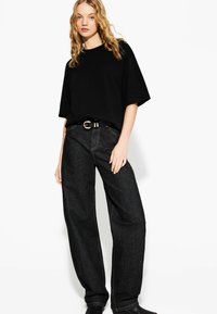 T-shirt nera oversize abbinata a jeans a gamba larga in denim scuro a vita alta. L'outfit presenta una cintura con fibbia dorata e una texture liscia e setosa.