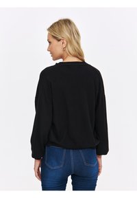 Czarny, oversize sweter z opadającymi ramionami, teksturowana tkanina i luźny krój, zestawiony z niebieskimi dżinsami z tylnymi kieszeniami.
