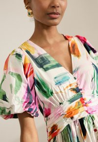 Robe florale colorée avec un décolleté en V profond, de grandes manches bouffantes et un détail de taille froncée agrémenté de boutons multicolores.