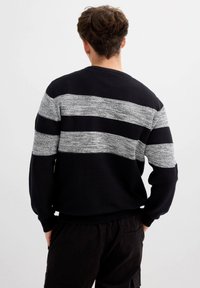 Jersey de punto en azul marino con rayas anchas grises. Presenta un patrón texturizado y puños y bajo acanalados. Vista desde atrás.