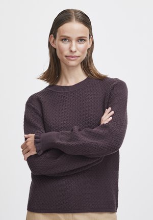 Lila gestrickter Pullover mit einem strukturierten Muster, rundem Halsauschnitt und langen, leicht puffigen Ärmeln. Der Stoff wirkt weich und warm.