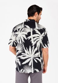 Camicia a maniche corte nera con grande stampa di palme bianche. Presenta un colletto alla camicia e una vestibilità rilassata, realizzata in tessuto leggero.