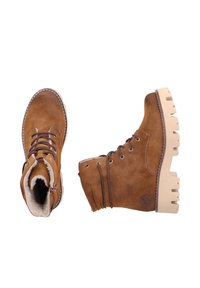 Brązowe zamszowe botki za kostkę z białym sztucznym futrem, sznurowanym wzorem oraz masywną beżową podeszwą z wyraźnym bieżnikiem.