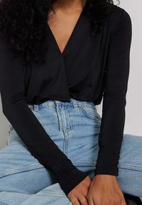 Top nero a maniche lunghe con scollo a V profondo, abbinato a jeans in denim azzurri a vita alta. Il tessuto appare liscio con una silhouette aderente.