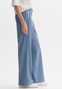 Pantalons à large jambe en tissu bleu clair avec une texture subtile, dotés de plis sur le devant et d'une taille haute, associés à des baskets blanches.
