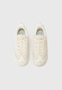 Sneakers in cream and white with a textured fabric upper, contrasting silver side accents, and a thick rubber sole. Laces are light beige.
