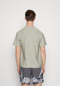 Ljusgrön, kortärmad T-shirt med en texturerad kvalitet, avslappnad passform och rund halsringning, tillsammans med grå shorts med ett grafiskt mönster.