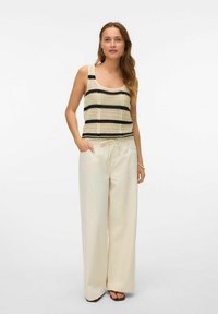 Gehaakte tanktop met zwarte en crèmekleurige strepen, gecombineerd met losse, lichtbeige broek. De broek heeft een elastische tailleband.